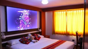 A hotel room with a bed, a large TV screen, a window with curtains, and a chair. - Mirador All Sur Cusco - Santa Ana (Cusco)
