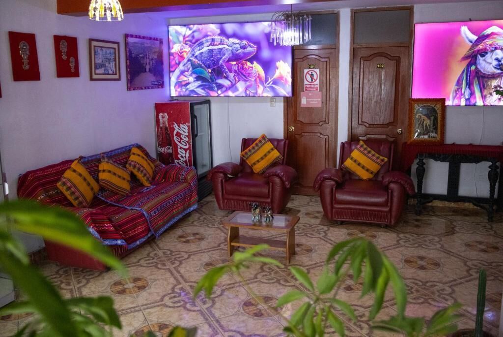 Una sala de estar con sofá, dos sillones, una mesita de centro, televisión y una puerta con un cartel.