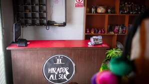 A reception desk with a sign reading 'Mirador All Sur,' a red counter, a shelf with decorative items, and a 'Bottiquin' sign. - Mirador All Sur Cusco - Santa Ana (Cusco)