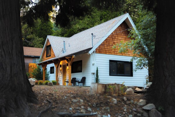 Een chalet met schuin dak, houten bekleding en een overdekte veranda met stoelen.