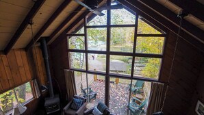 A cozy cabin with a large window, wooden walls, a ceiling fan, and a fireplace. - Lakeside Adirondack Resort-Cabin 7A (Olmstedville)