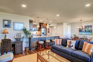A modern living room with a sofa, a glass coffee table, and a dining area with chairs. - Sea Gull #202LK: Beachfront 1 Bedroom 1 Bathroom With Spectacular Views and 24 Hour Management (Port Aransas)