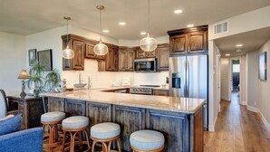 Una cocina con armarios de madera, una isla central con taburetes, luces colgantes y electrodomésticos de acero inoxidable.