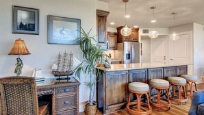Una cocina con armarios de madera, una isla central con taburetes, luces colgantes y cuadros en la pared.
