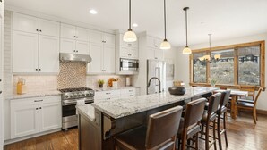 Una cocina moderna con armarios blancos, una isla central, electrodomésticos de acero inoxidable e iluminación colgante.