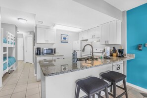 A modern kitchen with white cabinets, a granite countertop, and a blue accent wall.
