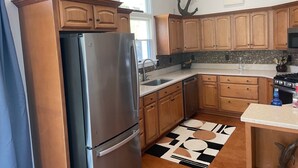 A kitchen with wooden cabinets, a stainless steel refrigerator, a tiled backsplash, and a patterned rug. - New Rental ~ Spacious Beach House - Hot Tub ~ Walk to the Beach (Kitty Hawk)