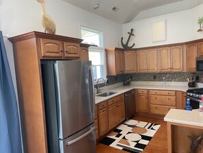 A kitchen with wooden cabinets, a stainless steel refrigerator, a tiled backsplash, and a patterned rug. - New Rental ~ Spacious Beach House - Hot Tub ~ Walk to the Beach (Kitty Hawk)