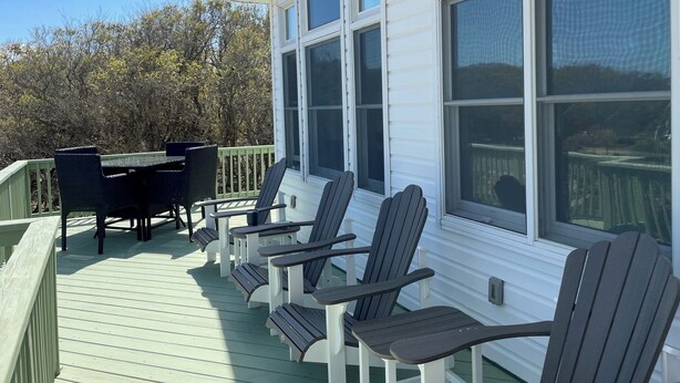 A covered deck with Adirondack chairs and a table, overlooking a body of water. - New Rental ~ Spacious Beach House - Hot Tub ~ Walk to the Beach (Kitty Hawk)