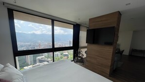 Ein Schlafzimmer mit großem Fenster, einem Bett, einem Fernseher und einem kleinen Tisch.