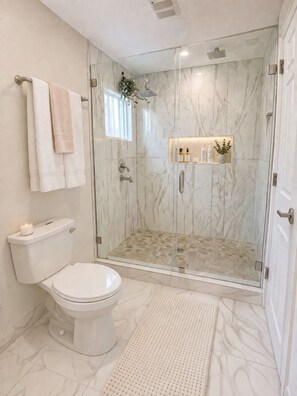 Ein modernes Badezimmer mit einer Glaskabine zur Dusche, einer Toilette und einem Waschtisch mit einem Regal für Pflegeprodukte.