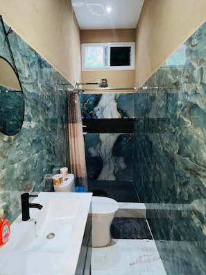 A bathroom with a marble wall, a white sink, a toilet, and a shower area.