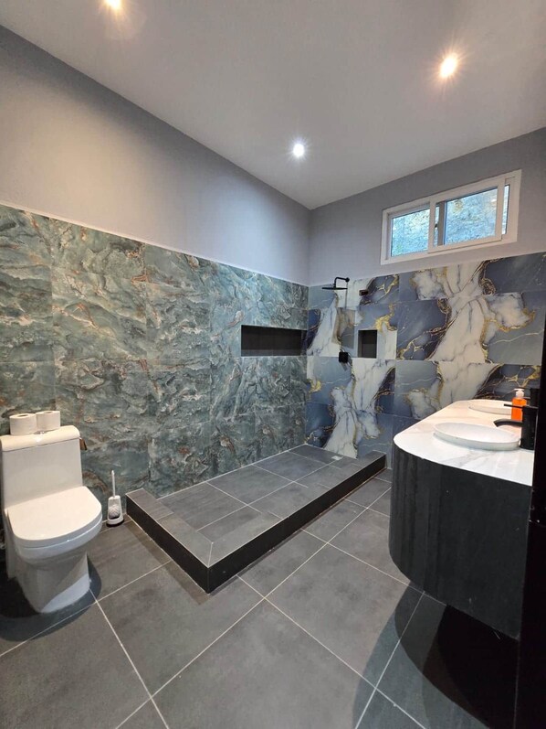 A modern bathroom with a marble wall, a shower, and a vanity.