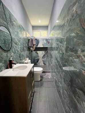 Une salle de bain avec un mur en marbre, un lavabo, des toilettes et un espace douche.