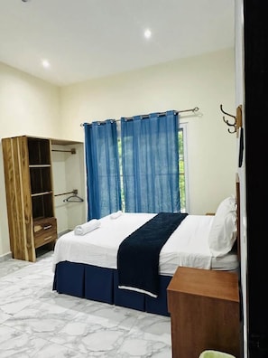A bedroom with a bed, a wardrobe, a mirror, and a window with curtains.