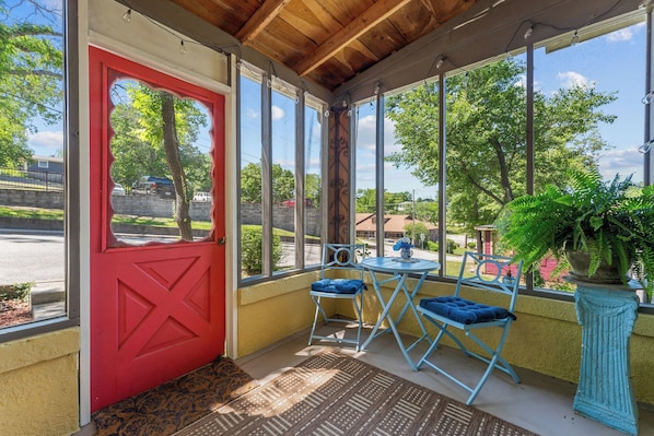 A covered porch with a red door, a small table with blue chairs, and a potted plant.