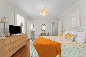 Une chambre à coucher avec un lit, une commode, une télévision et un miroir.