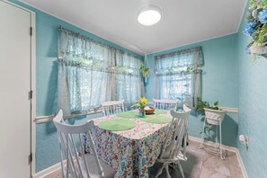 Un coin repas avec une table dressĂ©e pour quatre personnes, entourĂ©e de chaises blanches et recouverte dâune nappe Ă motifs floraux.