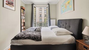 Een net opgemaakt bed met een gebloemd dekbed, een bedlampje en een boekenplank.