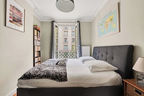 A neatly made bed with a patterned blanket, a bedside lamp, and a bookshelf. - T3 10 min from Rolland Garros & Parc des Princes (Paris)