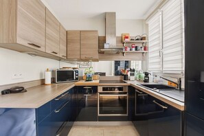 A modern kitchen with wooden cabinets, a built-in oven, and a window with blinds. - T3 10 min from Rolland Garros & Parc des Princes (Paris)