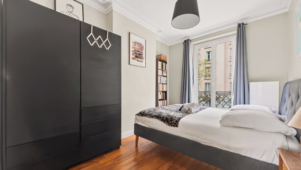 Een slaapkamer met een bed, een garderobe, een hanglamp en een raam met gordijnen.