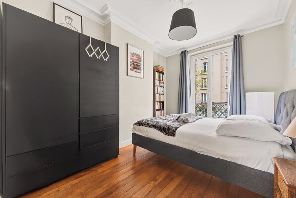 A bedroom with a bed, a wardrobe, a hanging light fixture, and a window with curtains. - T3 10 min from Rolland Garros & Parc des Princes (Paris)