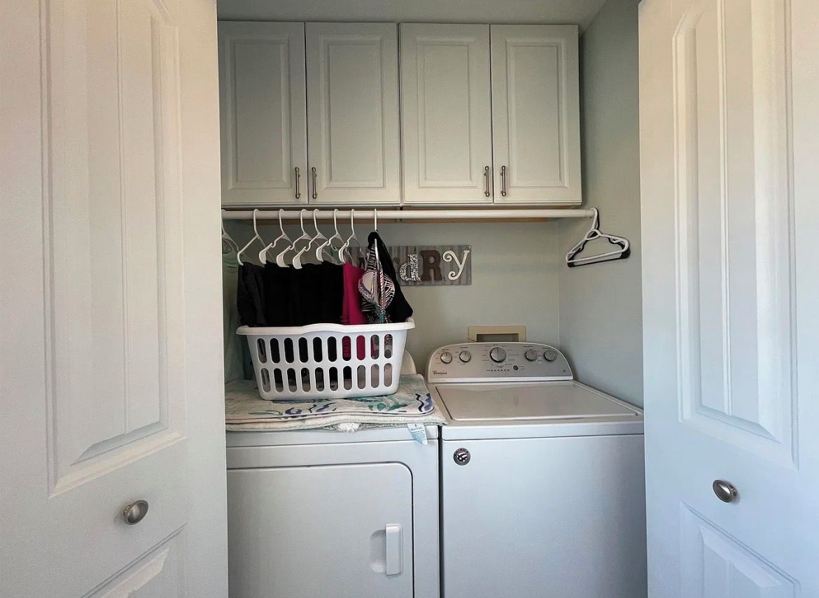 A laundry area with a washing machine, a dryer, and a basket of clothes on a shelf.