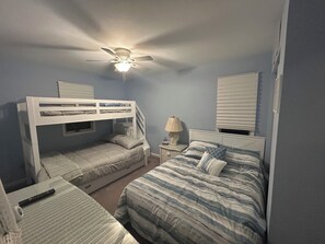 A bedroom with bunk beds, a single bed, a nightstand, a lamp, and a ceiling fan. - A Coastal Escape. 
Modern Marina district condo in delightful Wildwood (Wildwood)