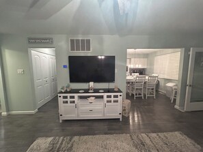 A living room with a flat-screen TV, a white entertainment unit, and a dining area with a chandelier. - A Coastal Escape. 
Modern Marina district condo in delightful Wildwood (Wildwood)