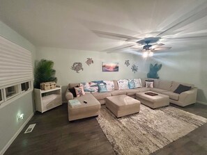 A living room with a sectional sofa, two ottomans, a ceiling fan, and decorative wall art. - A Coastal Escape. 
Modern Marina district condo in delightful Wildwood (Wildwood)