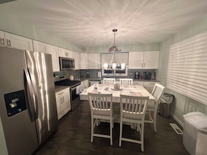 A modern kitchen with white cabinetry, stainless steel appliances, and a dining area with white chairs. - A Coastal Escape. 
Modern Marina district condo in delightful Wildwood (Wildwood)