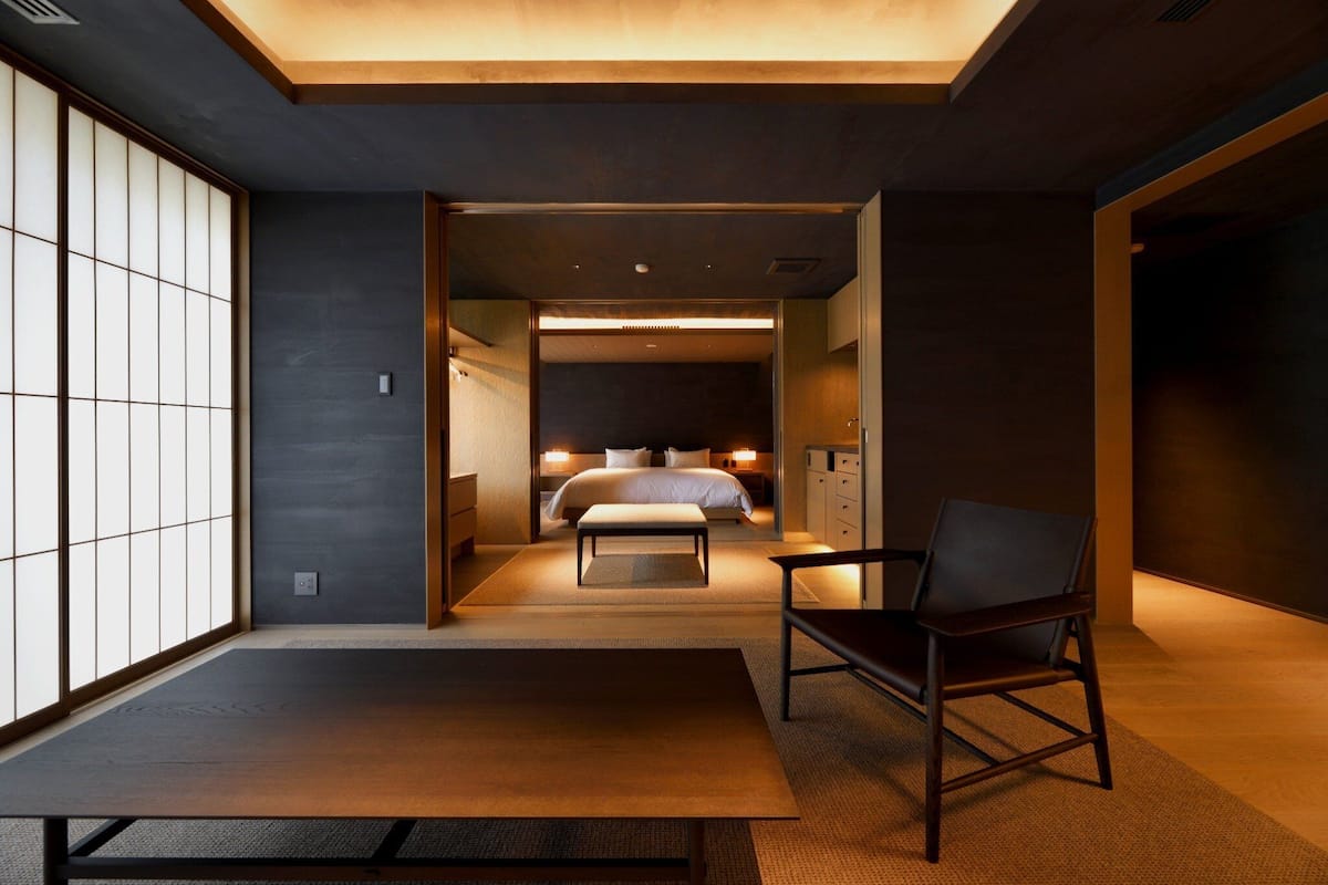 Una habitación de hotel moderna con una cama, una silla y vistas a través de un ventanal corredero.