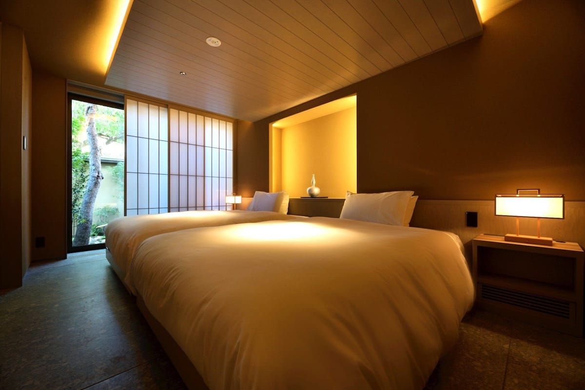 Una habitación de hotel con una cama grande, lámparas de noche, vistas a través de una puerta corredera y techo de madera.