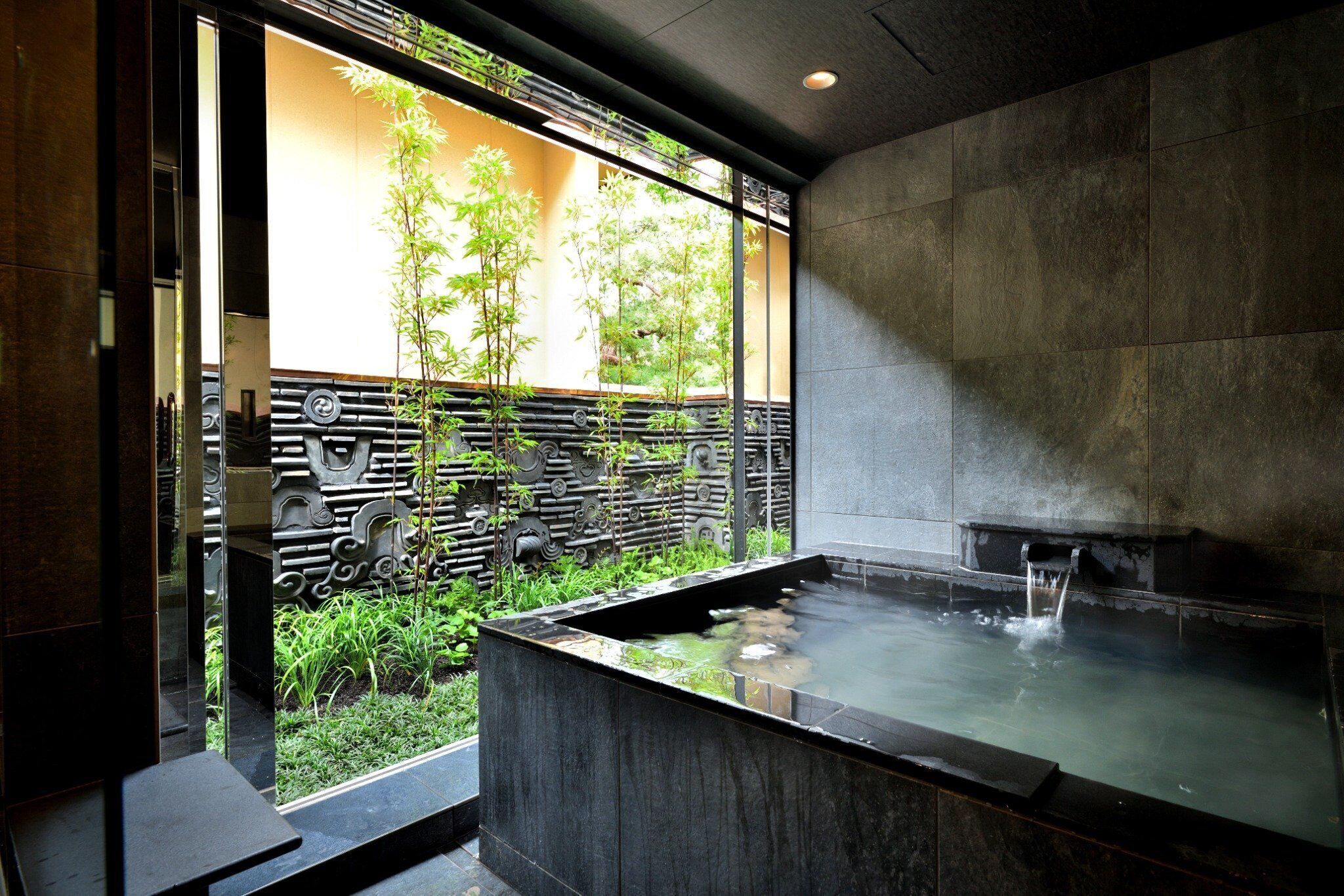 Un espace bien-être comprenant un jacuzzi, un mur en pierre et une vue sur la verdure environnante.