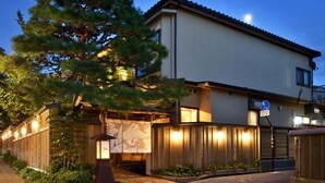 Un bâtiment moderne doté d’une entrée de style japonais traditionnel, d’un grand arbre et d’un chemin bien éclairé.