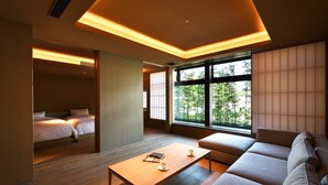 Une chambre d’hôtel moderne, dotée d’un canapé, d’une table basse en bois, d’un lit et de grandes fenêtres donnant sur un paysage verdoyant.