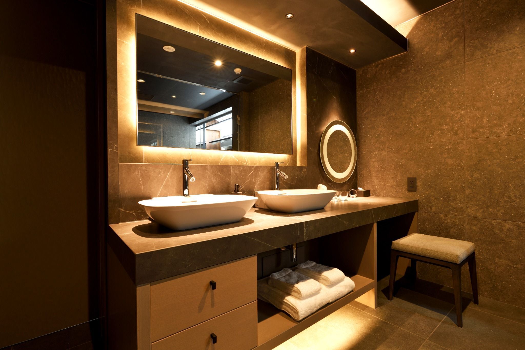 Un baño moderno con dos lavamanos, un espejo grande y un banco.