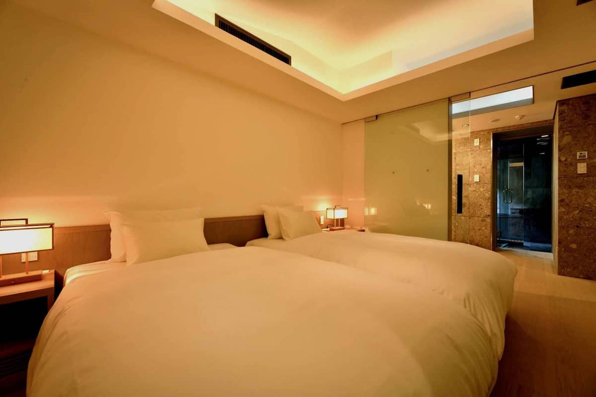 Una habitación de hotel con una cama grande, lámparas de noche, un espejo y una puerta que da a un baño.