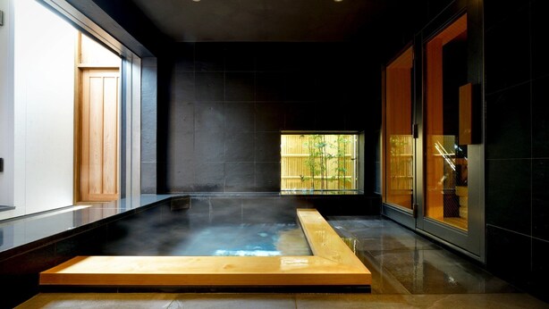 Une salle de spa moderne dotée d’un jacuzzi, de murs aux couleurs sombres et d’une grande fenêtre donnant sur un paysage verdoyant.