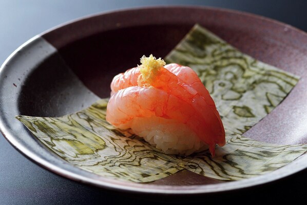 A sushi dish on a ceramic plate with a leaf garnish. - Tsuruko (Kanazawa)