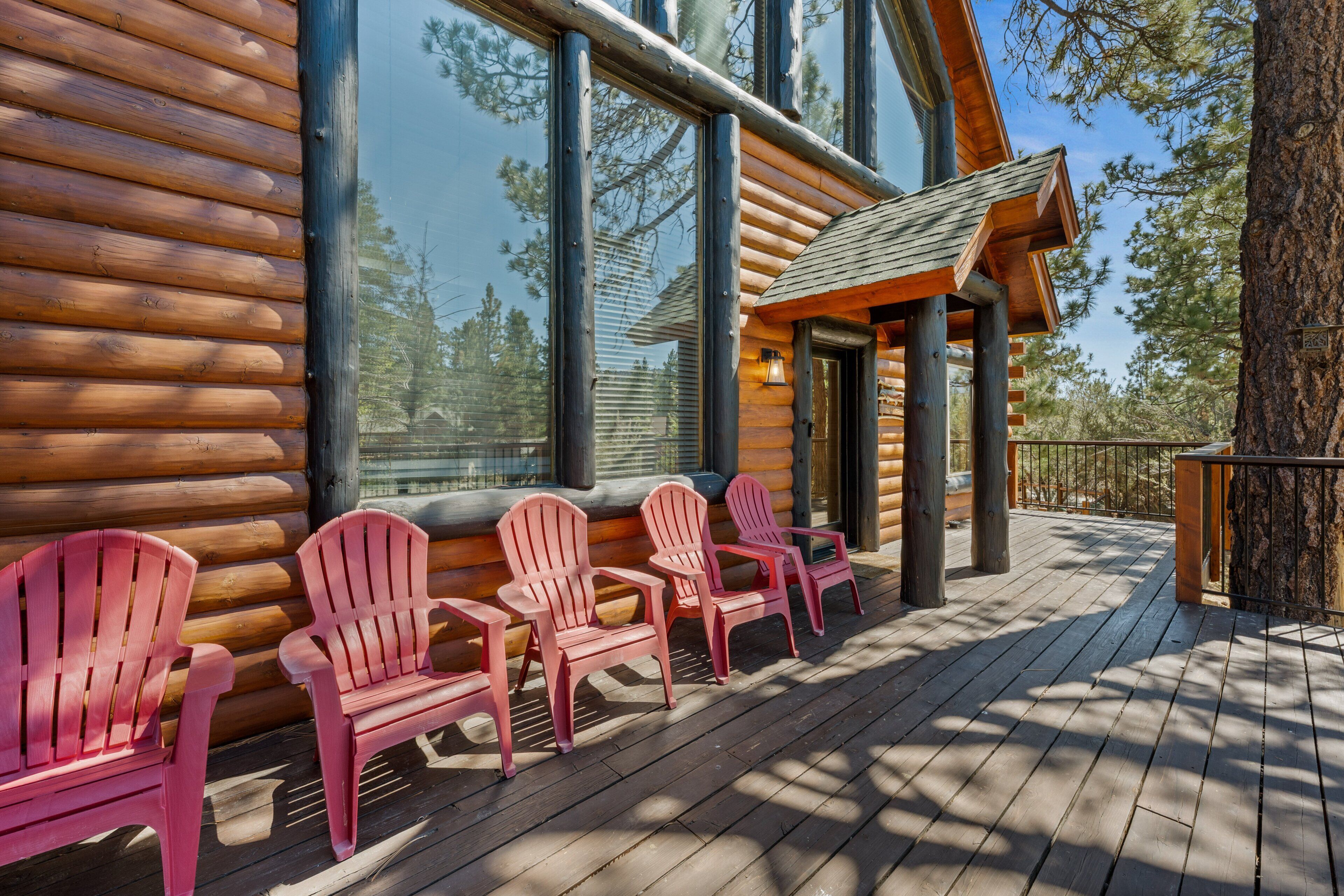 Une cabane en rondins dotée d’une terrasse avec des fauteuils Adirondack rouges et de grandes fenêtres.