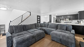 Una sala de estar moderna con un sofá seccional, una escalera y una zona de cocina.