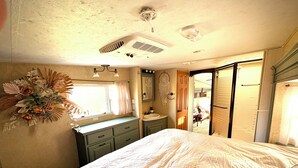 Ein Schlafzimmer mit einem Bett, einem Fenster mit Vorhängen, einem Waschbecken und einem Spiegel.