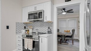 Een keuken met witte kastjes, een magnetron, een oven en een eethoek met een tafel en stoelen.