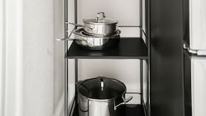 Een smalle keuken met een zwart metalen schap waarop keukengerei en een potplant staan.