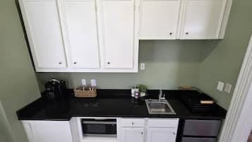 Una cocina compacta con armarios blancos, encimera negra, horno empotrado y pileta de acero inoxidable.
