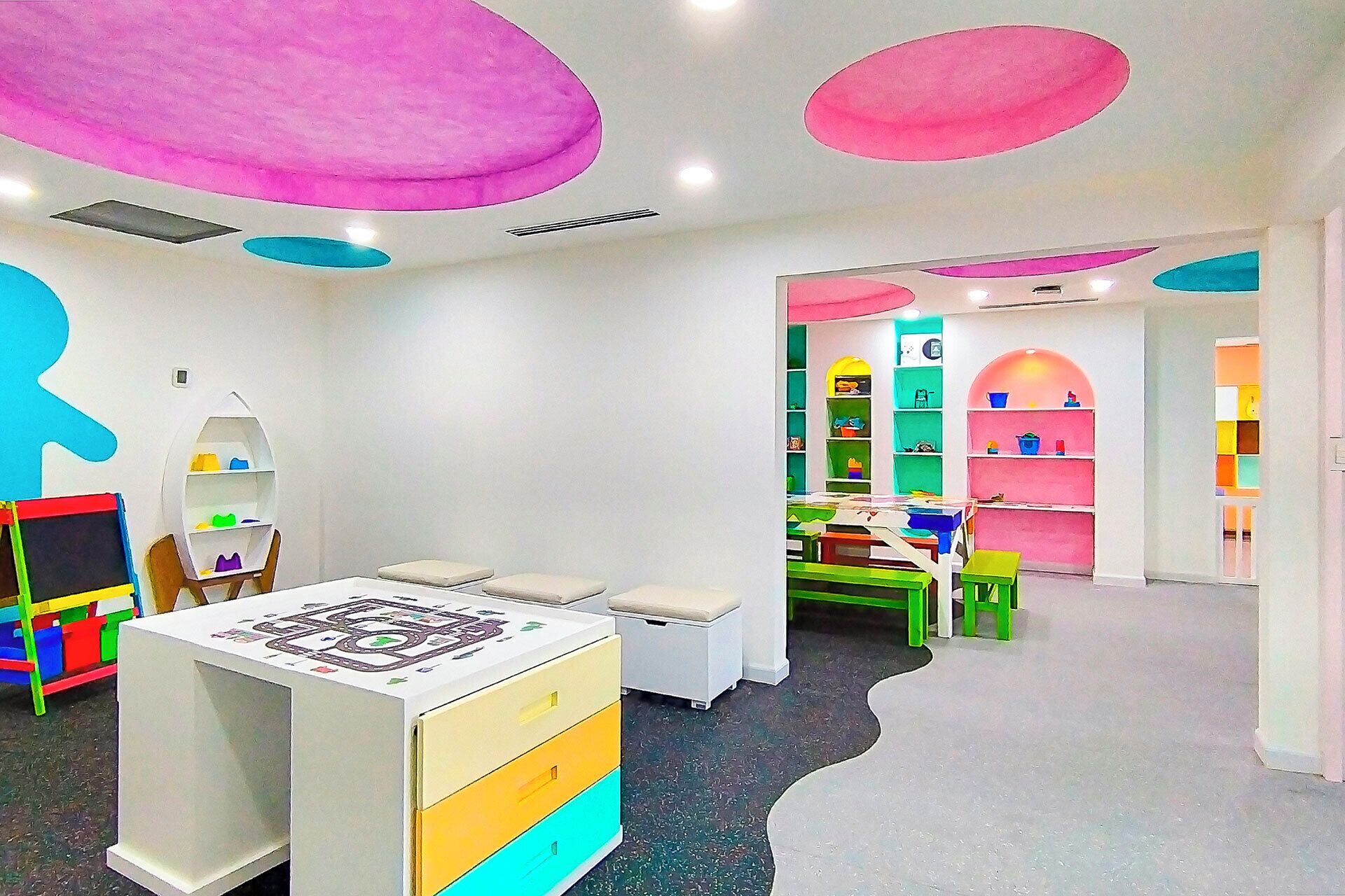 Een vrolijk ingerichte kinderspeelkamer met een grote tafel, stoelen en planken vol speelgoed.