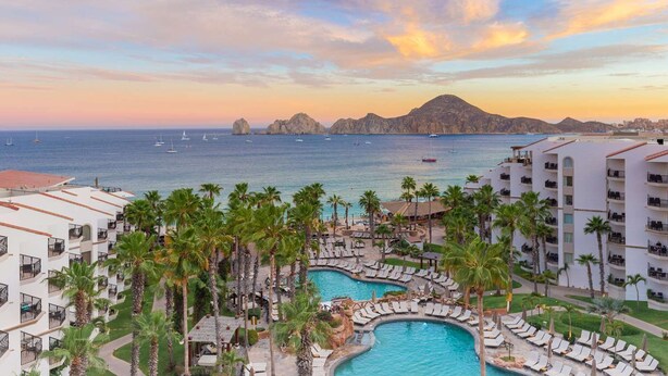 A resort with multiple swimming pools, palm trees, and a view of the sea and mountains. - Cabo San Lucas oceanfront getaway with resort amenities (Cabo San Lucas)