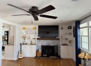 Ein Wohnzimmer mit Kamin, Deckenventilator und Fernseher.